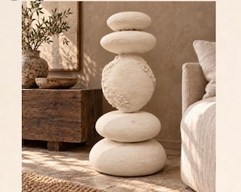 May include: A tall sculpture composed of five stacked, rounded, off-white stone-like shapes with a textured, matte finish. The central element features a rough, cratered surface, while the other four pieces are smooth and oval.