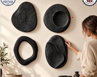 May include: A set of four black wall-mounted sculptures with irregular, organic shapes and textured surfaces. The pieces include a solid form, a circular recessed form, an open ring shape, and a layered, curved form displayed on a wall.