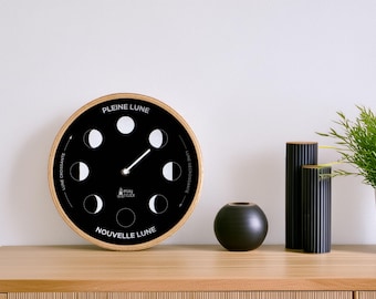 May include: A black and white moon phase clock with a wooden frame. The clock face shows the different phases of the moon, with the words "Pleine Lune" and "Nouvelle Lune" at the top and bottom.