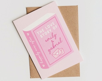 Pode incluir: Um cartão rosa com o texto "The Love Story of Emily & Gabriel" e uma ilustração de envelope em forma de coração. O cartão está em cima de um envelope castanho, com as palavras "happily ever after" impressas na lateral.