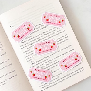 May include: Four rectangular pink stickers shaped like admission tickets, each featuring red strawberry illustrations and white text that reads ADMIT ONE STRAWBERRY PATCH pick your own strawberries, arranged on an open book page.