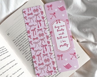May include: Two pink bookmarks with bow patterns and text. One bookmark features a repeating pattern of pink bows. The other has the text "buy me books and tell me i'm pretty" in a white frame, with bow and heart illustrations.