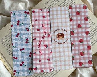 May include: Four decorative bookmarks with fruit and text designs. One has cherries on a blue and white checkered pattern. Another has strawberries and the text "Just let me adore you". The third has pancakes and the text "pancakes for two I will always love you". The last has peaches.