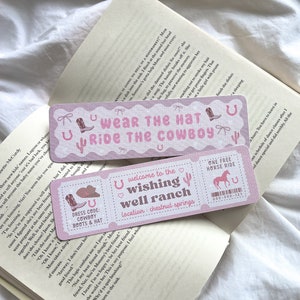 Puede incluir: Dos marcapáginas rosas con temática de vaqueros con texto e ilustraciones. Uno dice "Wear the Hat Ride the Cowboy" y el otro "Welcome to the Wishing Well Ranch" con un código de vestimenta "Cowboy Boots & Hat".