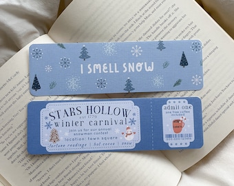 May include: Two blue bookmarks with winter-themed designs. One says "I SMELL SNOW" with snowflakes and trees. The other is a ticket for the "STARS HOLLOW winter carnival" with a snowman and "Luke's" coffee.