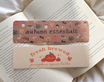 May include: Two rectangular bookmarks with autumn-themed designs. One bookmark reads "autumn essentials" with fall-themed illustrations. The other says "fresh brewed pumpkin spice latte" with a smiling pumpkin.