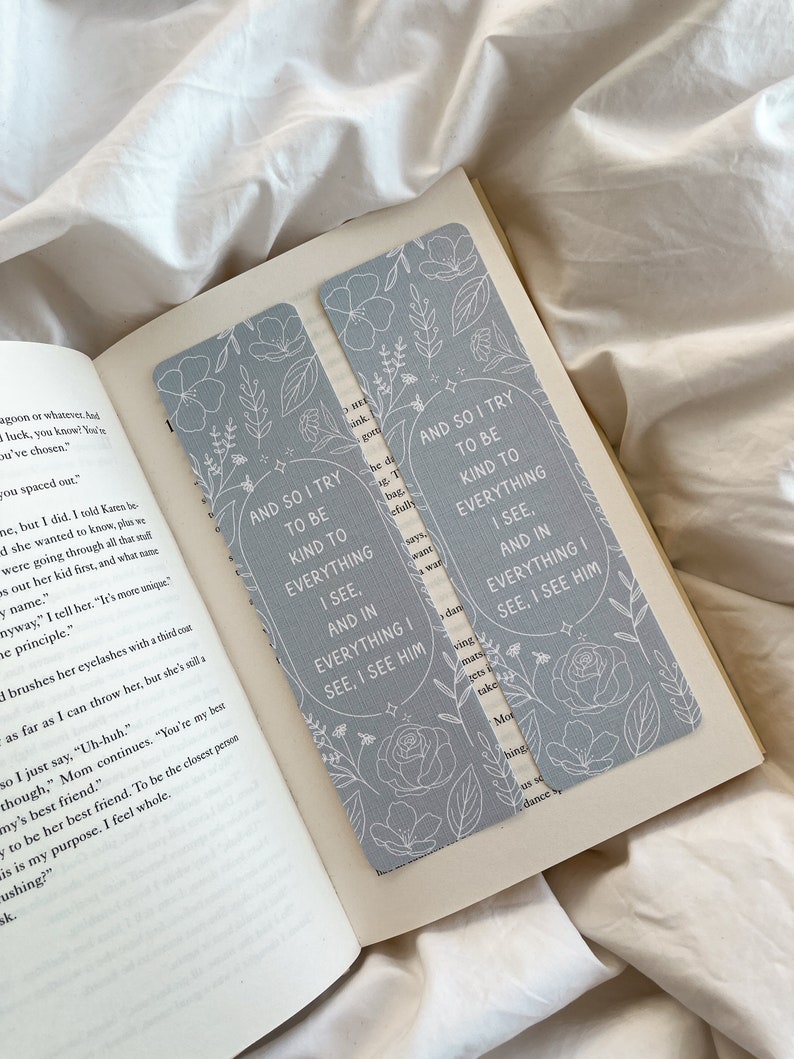 Puede incluir: Dos marcap&aacute;ginas gris claro con dise&ntilde;os florales y el texto "AND SO I TRY TO BE KIND TO EVERYTHING I SEE, AND IN EVERYTHING I SEE, I SEE HIM." Los marcap&aacute;ginas est&aacute;n en un libro abierto.