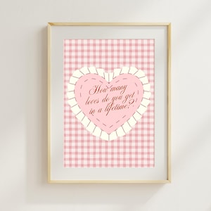 May include: Framed print featuring a pink gingham background. A pink heart with a white scalloped border is centered, displaying the text: "How many loves do you get in a lifetime?" The print is in a light wood frame.