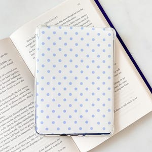 May include: A rectangular e-reader case featuring a white background with a repeating pattern of small, light blue polka dots. The case has a clear, transparent protective border that frames the dotted design on the front surface.