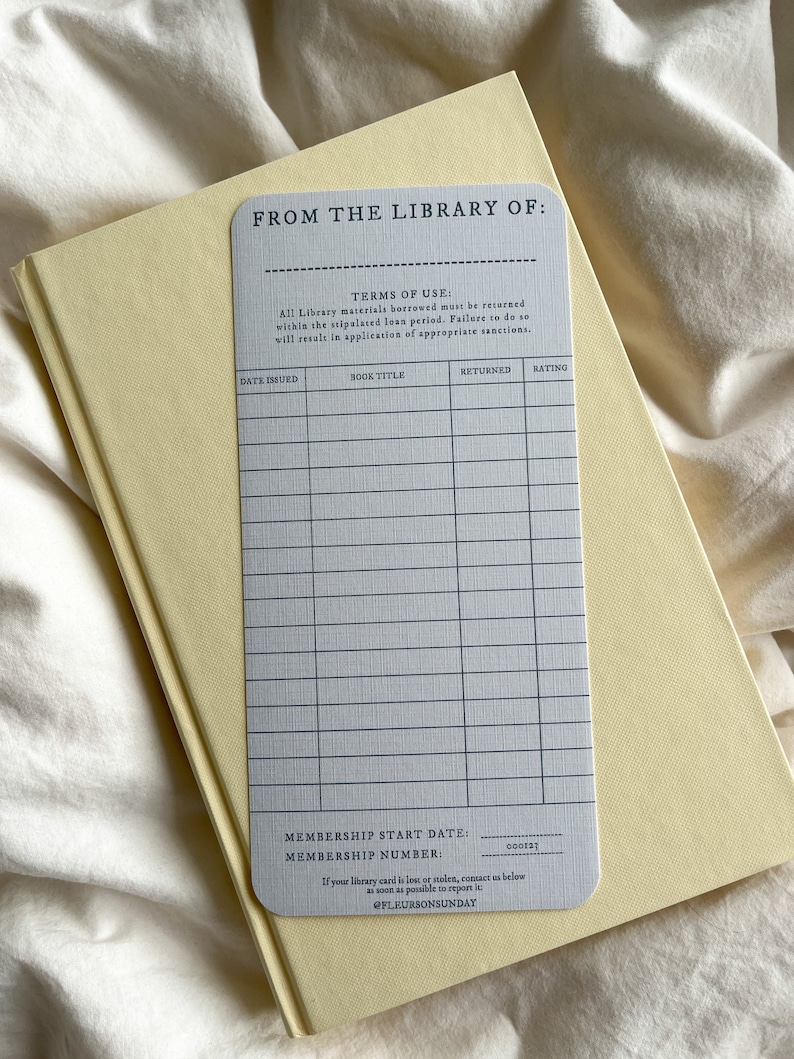 K&ouml;nnte beinhalten: Eine hellgraue Bibliothekskarte mit dem Text "FROM THE LIBRARY OF:" und einem Raster f&uuml;r Buchdetails, die auf einem hellgelben Buch liegt. Die Karte enth&auml;lt Felder f&uuml;r Ausgabedatum, Buchtitel, zur&uuml;ckgegeben und Bewertung. Der Text "@FLEURSONSUNDAY" befindet sich unten.