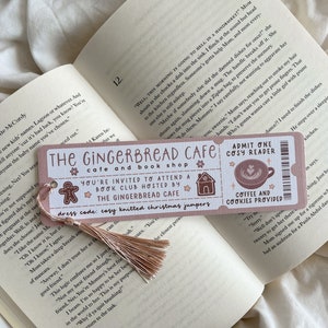 May include: A pink and white bookmark with the text "The Gingerbread Cafe" and "You're invited to attend a book club." It features a gingerbread man, a house, and a coffee cup illustration. A tassel hangs from the top.