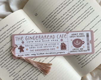 May include: A pink and white bookmark with the text "The Gingerbread Cafe" and "You're invited to attend a book club." It features a gingerbread man, a house, and a coffee cup illustration. A tassel hangs from the top.