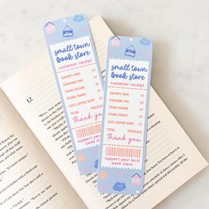 Op de afbeelding: Twee lichtblauwe bladwijzers met een bonontwerp, met de tekst "small town book store" en "customer receipt". De bladwijzers hebben een huis- en wolkenillustratie. De tekst "Thank you" en "support your local book store" zijn ook zichtbaar.