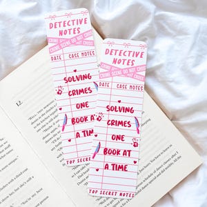 May include: Two pink and white detective-themed bookmarks with the text "Detective Notes" and "Solving Crimes One Book at a Time." The bookmarks feature a grid design with crime scene details and illustrations.