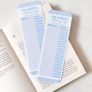 Op de afbeelding: Twee lichtblauwe bladwijzers met een gingham patroon rand en de tekst "my endless reading list". Elke bladwijzer heeft ruimte voor boektitels en hartvormige beoordelingen. De bladwijzers liggen op een open boek.