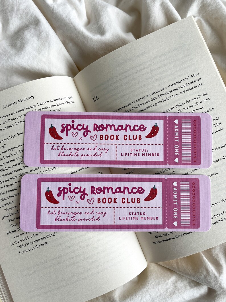 Pode incluir: Dois marcadores de livros retangulares cor-de-rosa com o texto "Spicy Romance Book Club" e uma ilustra&ccedil;&atilde;o de pimenta. Os marcadores tamb&eacute;m indicam "bebidas quentes e cobertores aconchegantes fornecidos" e o status "Membro Vital&iacute;cio".