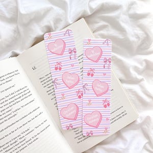 May include: Two rectangular bookmarks with a pink and purple striped background. Each bookmark features pink heart-shaped designs with names and the text "bj ballentine." Bows and ballet shoes are also included.