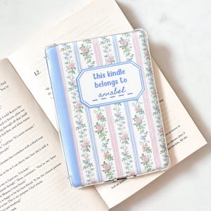 May include: A Kindle case with a floral pattern of pink and blue roses on a white background. The case has a blue border and the text "this kindle belongs to annabel" in a blue frame.