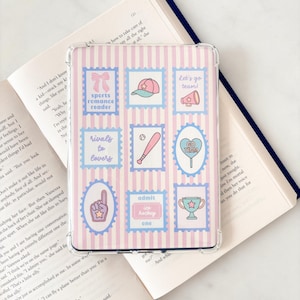 Puede incluir: Funda transparente para teléfono con un fondo a rayas rosas y blancas y varios gráficos temáticos deportivos. Incluye una gorra de béisbol, un bate de béisbol, un trofeo y texto que dice "Sports Romance Reader" y "Let's go team!"