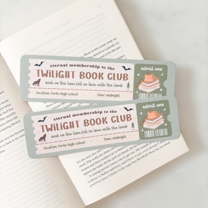 May include: Two pale green Twilight Book Club membership tickets featuring bats, a wolf, and a stack of books with a teacup. The tickets are placed on an open book with text.