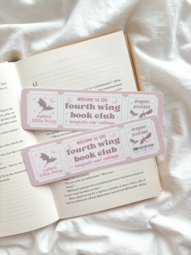Op de afbeelding: Twee roze bladwijzers met de tekst "Welcome to the Fourth Wing Book Club" en "Dragons Provided" liggen op een open boek. De bladwijzers hebben een vleermuis- en maanontwerp, met de woorden "violent little thing."