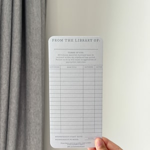 K&ouml;nnte beinhalten: Eine rechteckige Bibliothekskarte mit abgerundeten Ecken, vor wei&szlig;em Hintergrund gehalten. Die Karte tr&auml;gt den Text "FROM THE LIBRARY OF:" und einen Abschnitt f&uuml;r Buchdetails. Sie enth&auml;lt den Text "TERMS OF USE:" und die Mitgliedsnummer.