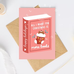 May include: A pink Christmas card with a book design. The card reads "All I want for Christmas is more books" with a stocking graphic. The words "happy holidays" are written vertically on the left side of the card. The card is on a brown envelope.