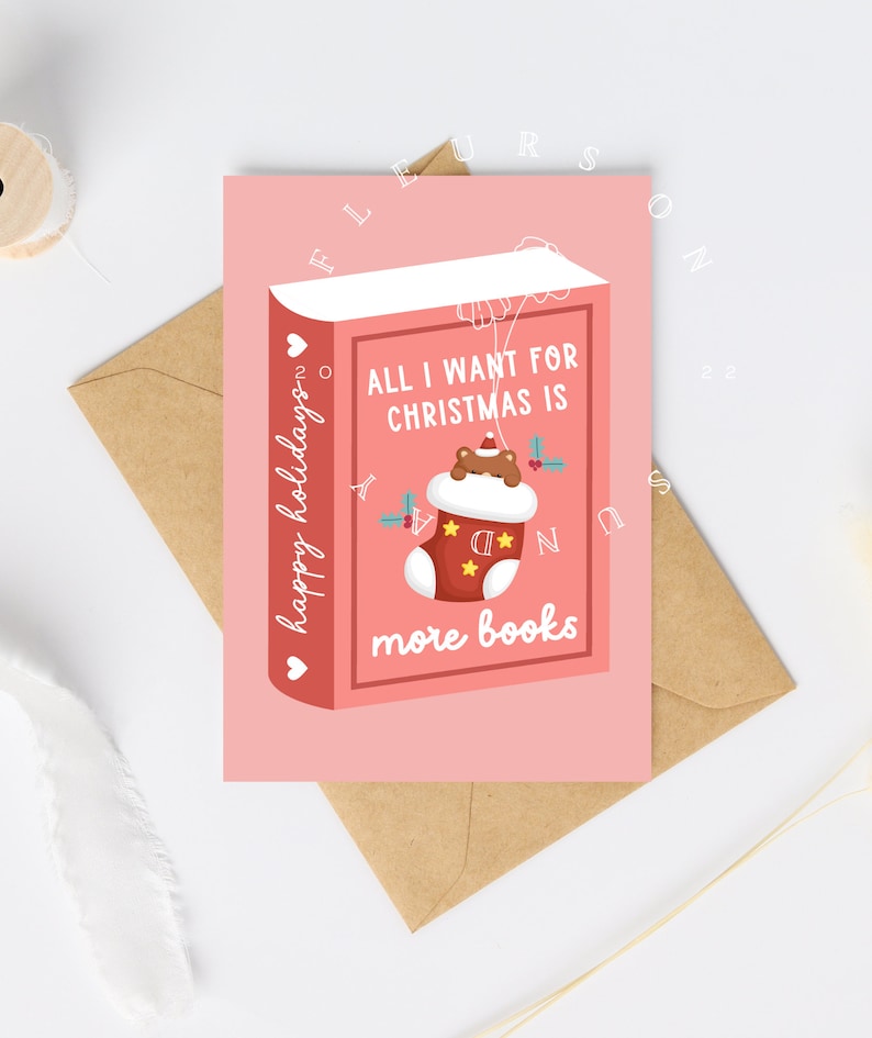 May include: A pink Christmas card with a book design. The card reads "All I want for Christmas is more books" with a stocking graphic. The words "happy holidays" are written vertically on the left side of the card. The card is on a brown envelope.