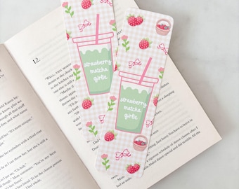 May include: Two decorative bookmarks with a pink and white gingham pattern. Each bookmark features a green drink with a pink straw, strawberries, flowers, and the text "strawberry matcha girlie."
