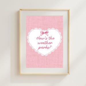 May include: A framed print with a pink background and a white heart-shaped design. The heart has a lace-like border and a pink bow at the top. The text "How's the weather parks?" is written in pink script inside the heart.