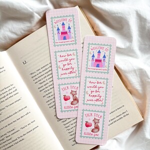 May include: Two pink bookmarks with fairytale castle and fox illustrations, resting on an open book. The bookmarks feature text that reads "Welcome to the magnificent north", "How far would you go for happily ever after?" and "Tick Tock little fox."