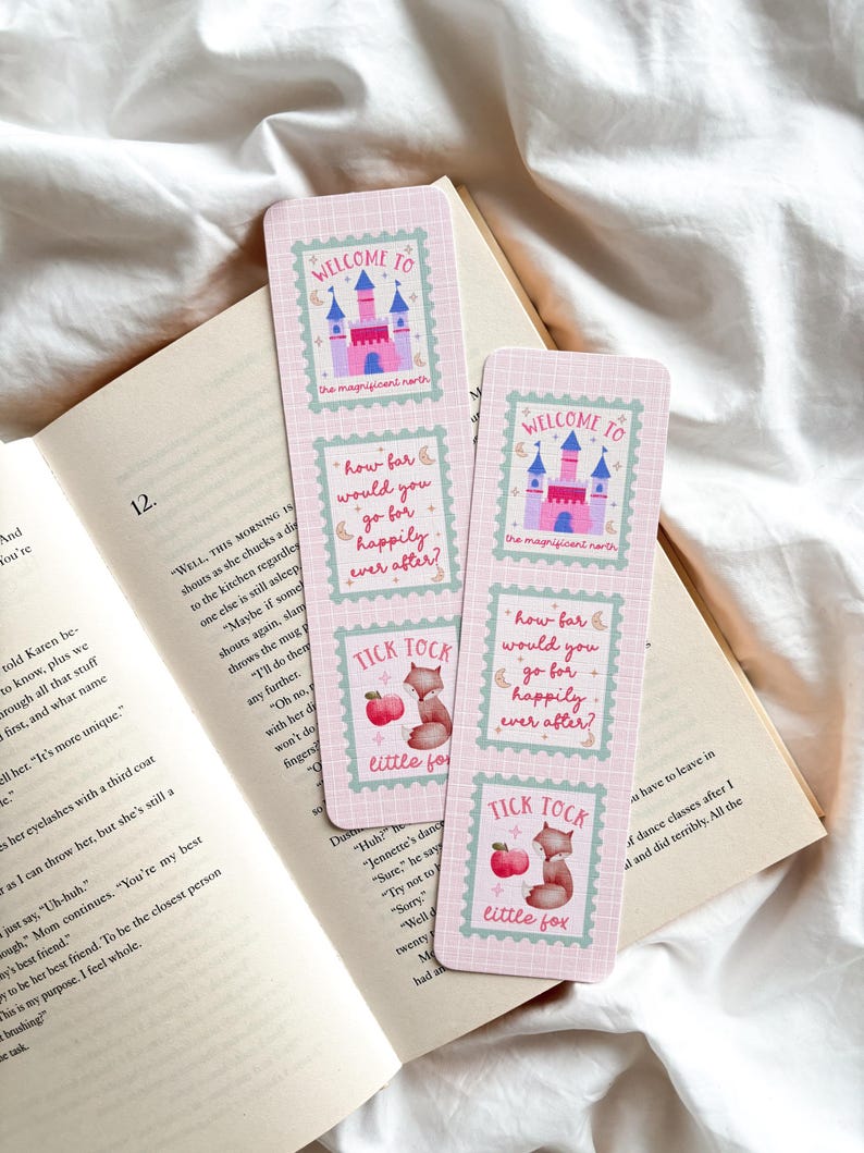 May include: Two pink bookmarks with fairytale castle and fox illustrations, resting on an open book. The bookmarks feature text that reads "Welcome to the magnificent north", "How far would you go for happily ever after?" and "Tick Tock little fox."