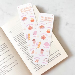 K&ouml;nnte beinhalten: Zwei rechteckige Lesezeichen mit dem Text "fall bookish essentials" und herbstlichen Illustrationen. Die Lesezeichen zeigen Bilder von K&uuml;rbissen, Bl&auml;ttern, B&uuml;chern und Kaffeetassen.