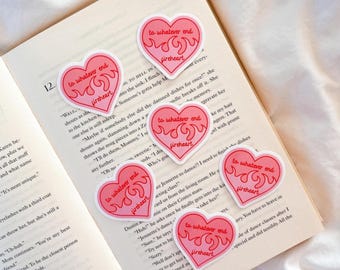 May include: A collection of six heart-shaped stickers with a pink and red flame design. Each sticker features the text "to whatever end" above "fireheart" in a handwritten style font. The stickers are placed on the open pages of a book.