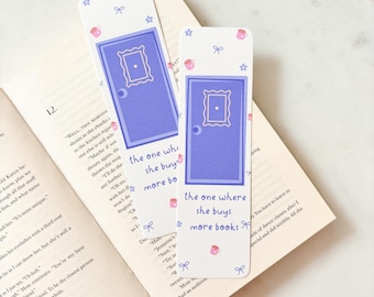 May include: Two white bookmarks with a purple door design and the text "the one where she buys more books" are placed in an open book. The bookmarks have pink teacups, bows, and stars.