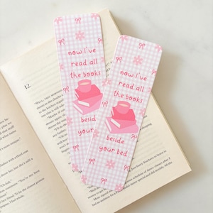 Puede incluir: Dos marcapáginas rosas y blancos a cuadros con el texto "now I've read all the books beside your bed". Cada marcapáginas presenta una pila de libros, una taza de té y detalles florales y lazos.