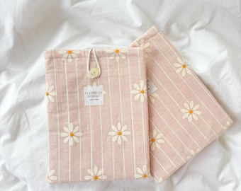 May include: Two pink fabric cases with white daisy embroidery and vertical stripes. One case is closed with a wooden button and string. The text "FLEURS ON SUNDAY" is printed on a small label. The cases are on a white sheet.