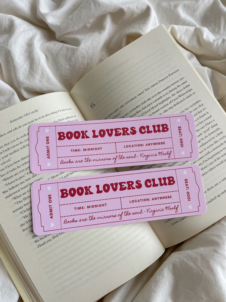 May include: Two pink ticket-shaped bookmarks with the text "BOOK LOVERS CLUB" in a bold, vintage font. The bookmarks are on top of an open book with white pages. The text "Books are the mirrors of the soul - Virginia Woolf" is also printed on the bookmarks.