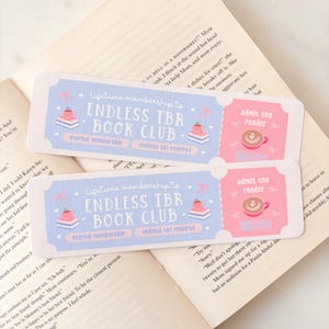 Peut inclure: Deux marque-pages décoratifs avec un design bleu clair et rose. Les marque-pages indiquent "ENDLESS TBR BOOK CLUB" et "admit one reader". Les marque-pages sont posés sur un livre ouvert.
