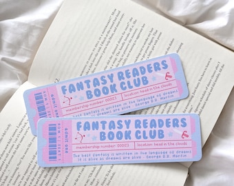 May include: Two pink and blue "Fantasy Readers Book Club" ticket-style stickers with the text "location head in the clouds" and a quote. The stickers are on top of an open book with text.