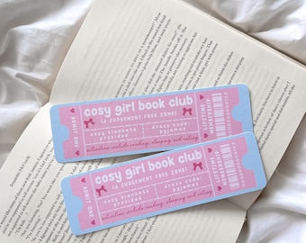 Puede incluir: Dos entradas rosas y azules de "cosy girl book club" con texto en un libro abierto. Las entradas tienen un lazo gráfico e indican "cosy blankets provided" y "dress code: pyjamas."
