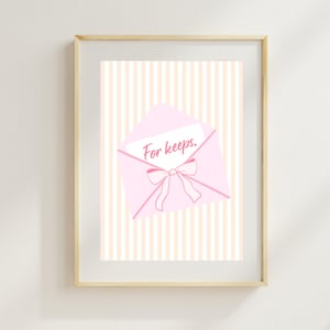 May include: Framed print showing a pink envelope with a bow and the words "For keeps." The envelope is set against a striped background of peach and white. The frame is a light wood colour.