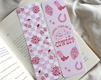 May include: Two decorative bookmarks. One features a pink and white checkered pattern with cherries, disco balls, and bows. The other has a pink background with cowboy-themed graphics and the text "CUPID, FIND ME A COWBOY."