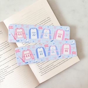 May include: Two hockey-themed bookmarks with light blue backgrounds and jersey designs. Each bookmark features a jersey with a name and number, hockey sticks, and ice skates. The names are Graham, Logan, Di Laurentis, and Tucker.