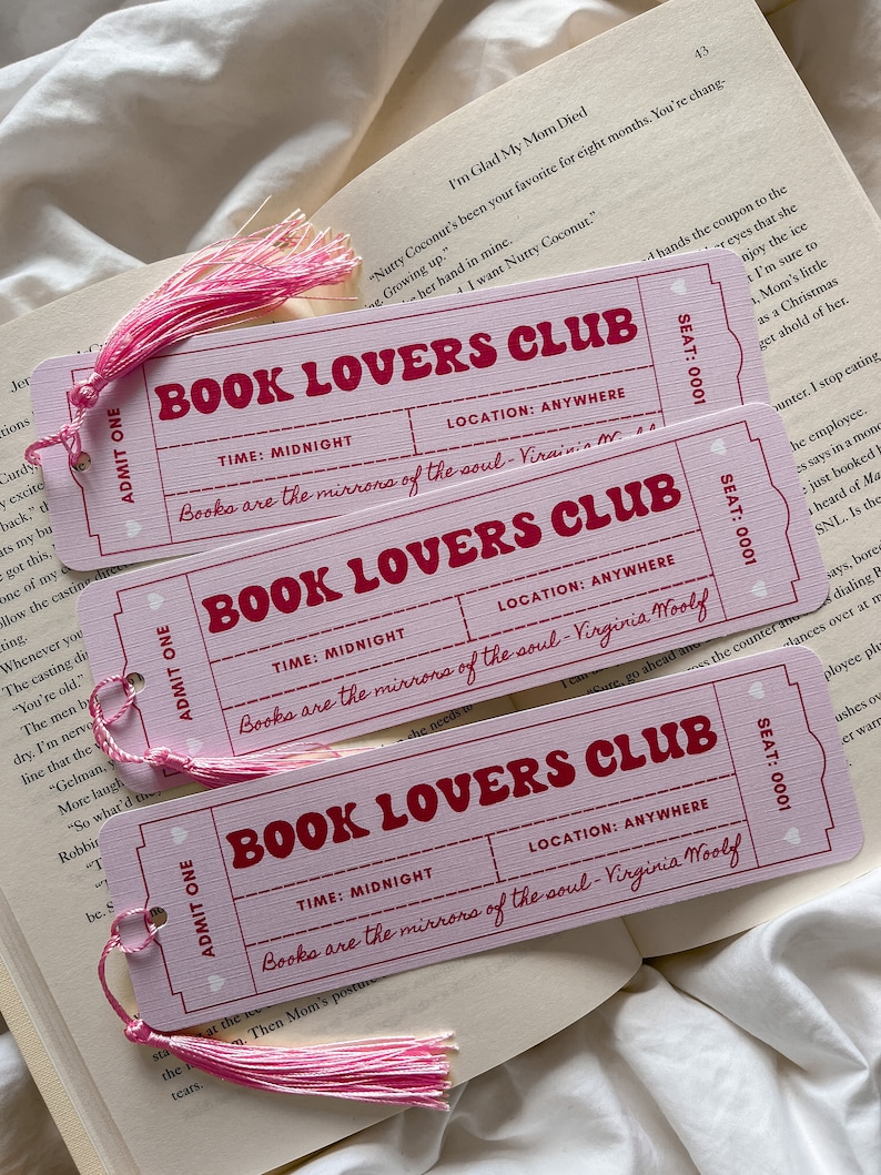 May include: Three pink bookmarks with the text "BOOK LOVERS CLUB" in red. Each bookmark has a pink tassel and the quote "Books are the mirrors of the soul - Virginia Woolf." The bookmarks are on top of an open book.