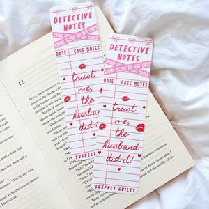 May include: Two detective-themed bookmarks with pink and red accents. The bookmarks feature the text "DETECTIVE NOTES" and "CRIME SCENE DO NOT CROSS." One bookmark reads "trust me, the husband did it!" with a lipstick kiss.