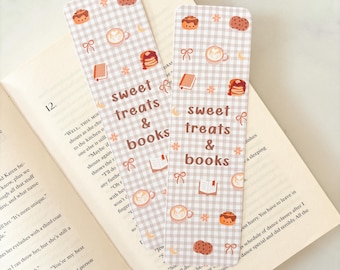 May include: Two rectangular bookmarks with a light brown gingham pattern, featuring illustrations of coffee cups, cookies, books, and bows. The text "sweet treats & books" is printed on each bookmark. The bookmarks are placed on an open book.