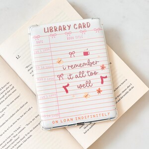 May include: Transparent phone case with a library card design. The case has a pink and white lined background with the words "Library Card" and "i remember it all too well" in a handwritten font. Decorative bows and floral accents are also included.
