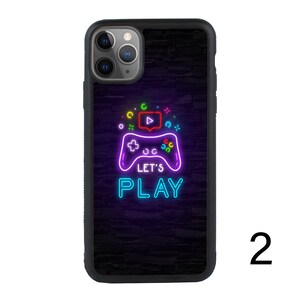 Puede incluir: Carcasa de tel&eacute;fono negra con un gr&aacute;fico de mando de videojuego verde ne&oacute;n, azul y rosa y el texto "Let's Play".