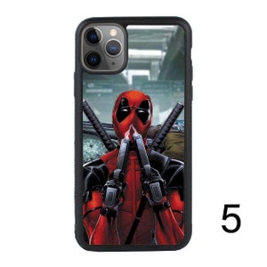 May include: Black phone case with a graphic of Deadpool holding two guns in front of his face. The background is a blurry image of a city street.